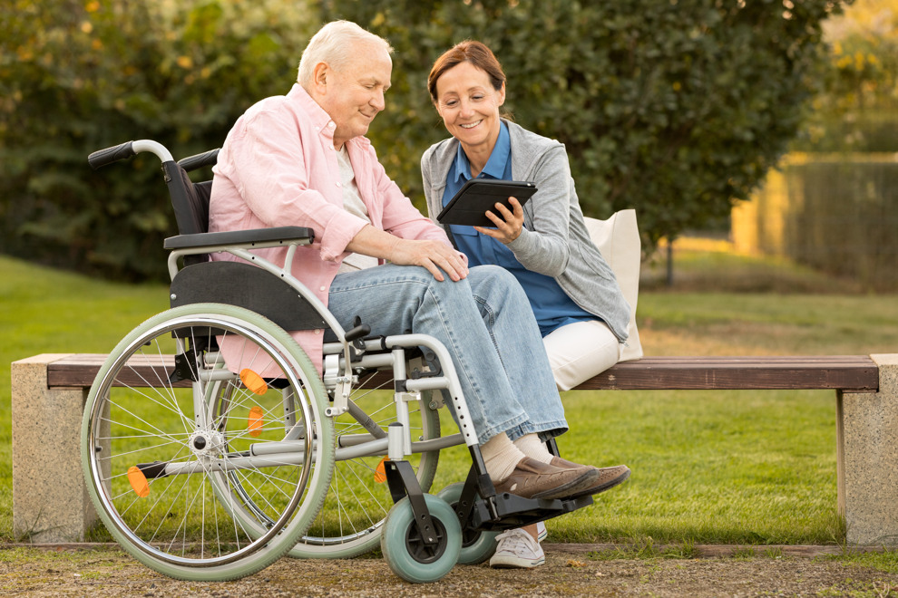 Man in wheelchair and woman looking at an ipad together. Image.