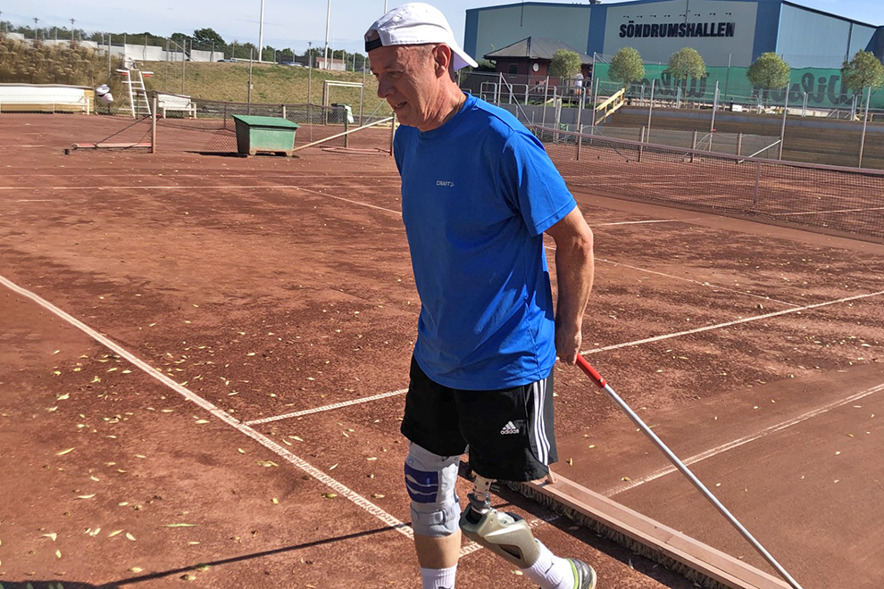 En man med benprotes på en tennisbana i grus. Bild.